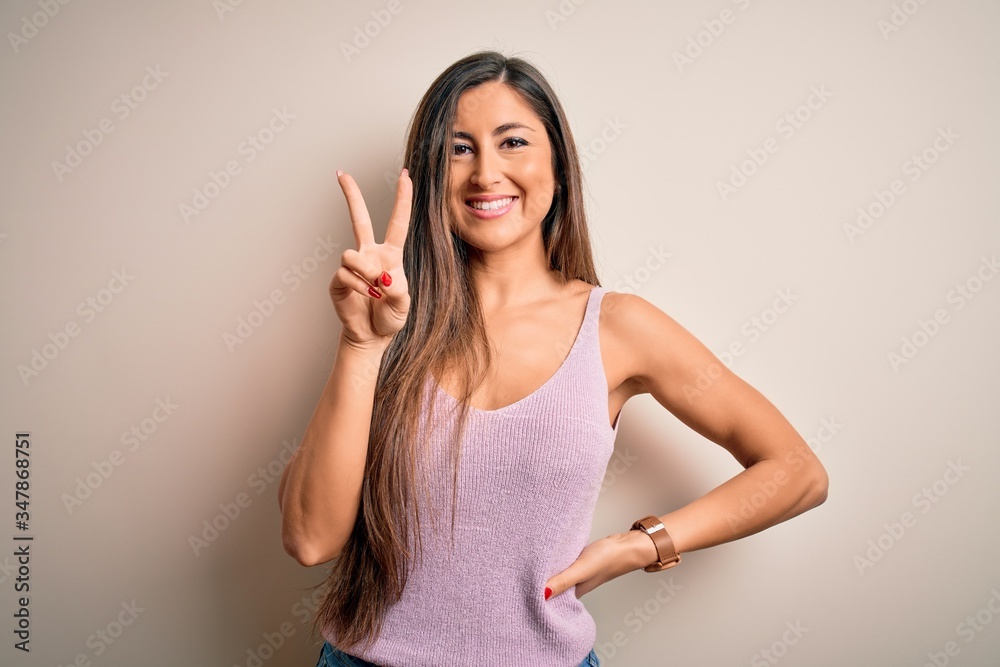 Young beautiful brunette woman with long hair standing over isolated background smiling with happy face winking at the camera doing victory sign. Number two. Young beautiful brunette woman with long hair standing over isolated background smiling with happy face winking at the camera doing victory sign. Number two.