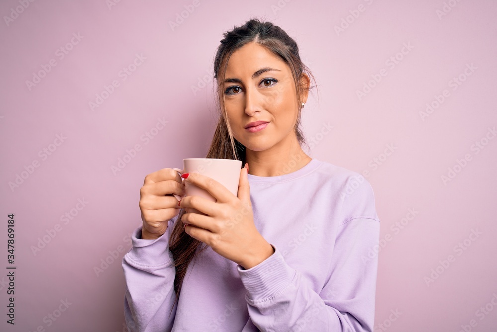 Young beautiful brunette woman drinking mug of coffee over isolated pink background with a confident expression on smart face thinking serious Young beautiful brunette woman drinking mug of coffee over isolated pink background with a confident expression on smart face thinking serious