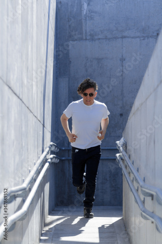 Man with curly hair and sunglasses running in a narrow concrete passageway photo