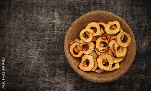 Apple ring chips in a wooden bowl and scattered on dark brown wooden background, table, copy space, top view