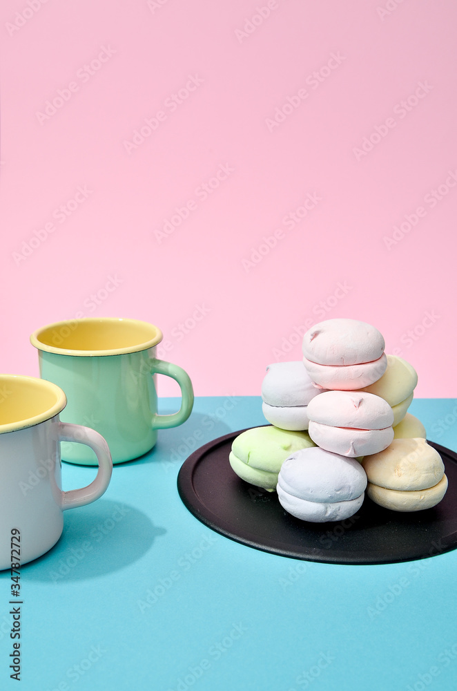 Top view of pastel colored marshmallow on black plate and two empty cups on a blue pink background. Minimalism photo for your design Top view of pastel colored marshmallow on black plate and two empty cups on a blue pink background. Minimalism photo for your design