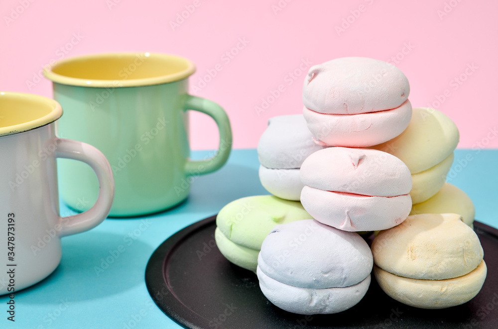 Top view of pastel colored marshmallow on black plate and two empty cups on a blue pink background. Minimalism photo for your design Top view of pastel colored marshmallow on black plate and two empty cups on a blue pink background. Minimalism photo for your design
