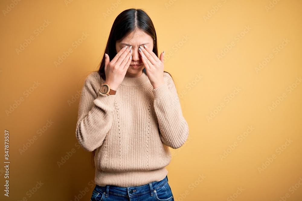 Young beautiful asian woman wearing casual sweater over yellow isolated background rubbing eyes for fatigue and headache, sleepy and tired expression. Vision problem Young beautiful asian woman wearing casual sweater over yellow isolated background rubbing eyes for fatigue and headache, sleepy and tired expression. Vision problem