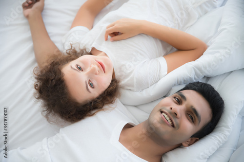 Handsome young men and beautiful women wearing white T-shirts They are smiling, looking and lying on the bed in the bedroom. The concept of morning sleep for lovers and love