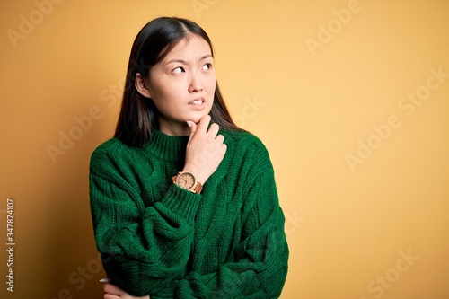 Young beautiful asian woman wearing green winter sweater over yellow isolated background Thinking worried about a question, concerned and nervous with hand on chin © Krakenimages.com