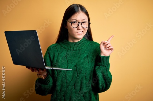 Young asian business woman wearing glasses and working using computer laptop Pointing aside worried and nervous with forefinger, concerned and surprised expression photo