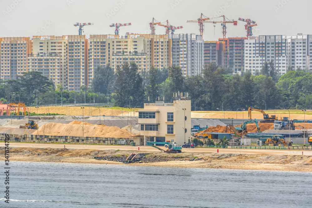 Φωτογραφία Backhoes and other land moving machinery perform land reclamation and ground improvement works at construction site of new public housing apartments on waterfront of Johor strait in Singapore