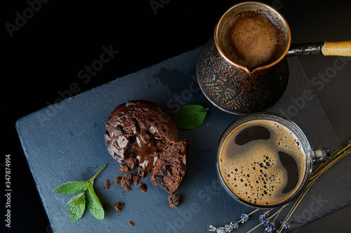 A delicious chocolate muffin, a cup of black coffee, a cezve with custard coffee. Decorated with mint and lavender.