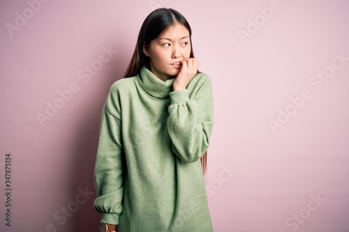 Young beautiful asian woman wearing green winter sweater over pink solated background looking stressed and nervous with hands on mouth biting nails. Anxiety problem. © Krakenimages.com
