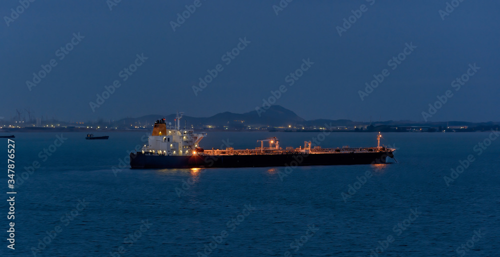 Crude oil tanker with navigation lights anchored in front of an oil storage terminal  at golden hour.