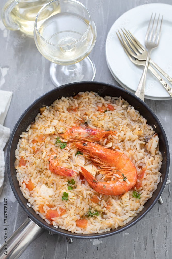 rice with fish and seafood in frying pan on ceramic background