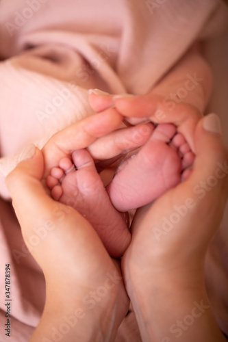 Baby feet in mother hands. Tiny Newborn Baby's feet on female Heart Shaped hands closeup. Mom and her Child. Happy Family concept. Beautiful conceptual image of Maternity.