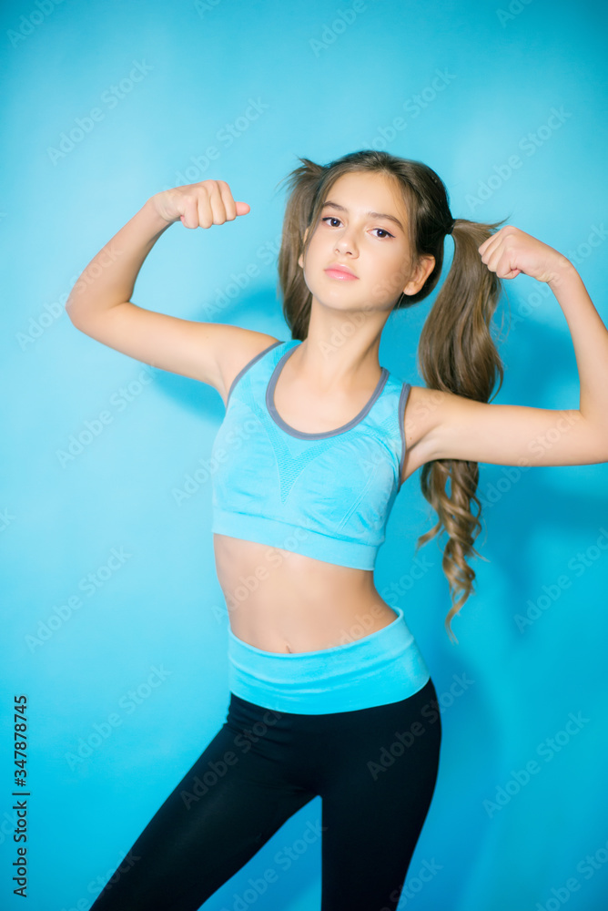 Cute teenager girl with long blond hair in fitness clothes on a blue background in the studio. Sports fashion. Sport for youth. Cute teenager girl with long blond hair in fitness clothes on a blue background in the studio. Sports fashion. Sport for youth.