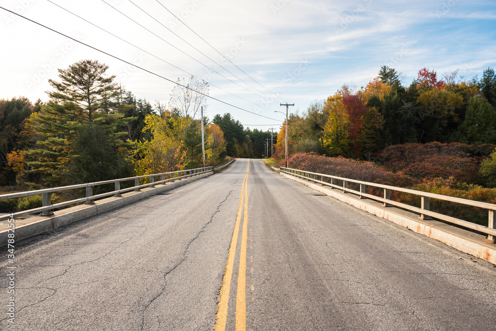 Empty bridge along a forest road in the countryside of Vermont at sunset in autumn