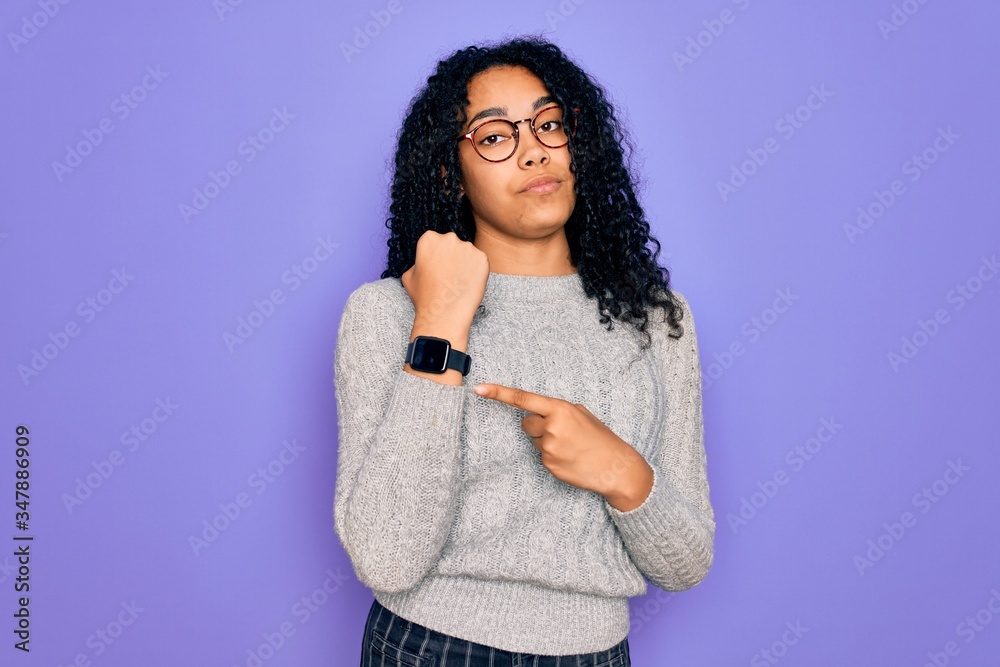 Young african american woman wearing casual sweater and glasses over purple background In hurry pointing to watch time, impatience, looking at the camera with relaxed expression Young african american woman wearing casual sweater and glasses over purple background In hurry pointing to watch time, impatience, looking at the camera with relaxed expression