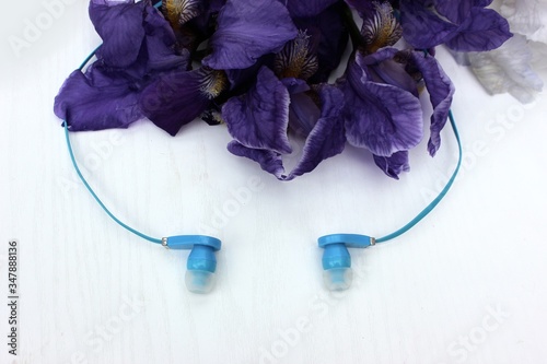 Obraz na płótnie Blue headphones isolated on white, in the background flowers. Blue earphone on a background of blue iris flowers isolated on white. Side view, copyspace w salonie