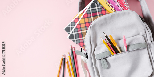 Back to school concept. Backpack with school supplies, pens, pencils, notebook on pastel pink background. Flat lay, top view, copy space