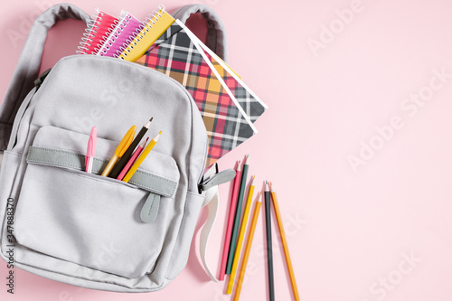 Back to school concept. Backpack with school supplies, pens, pencils, notebook on pastel pink background. Flat lay, top view, copy space