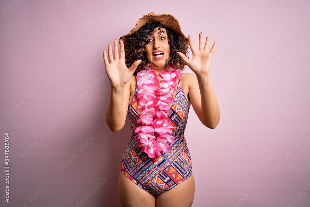 Young beautiful arab woman on vacation wearing swimsuit and hawaiian lei flowers afraid and terrified with fear expression stop gesture with hands, shouting in shock. Panic concept. Young beautiful arab woman on vacation wearing swimsuit and hawaiian lei flowers afraid and terrified with fear expression stop gesture with hands, shouting in shock. Panic concept.