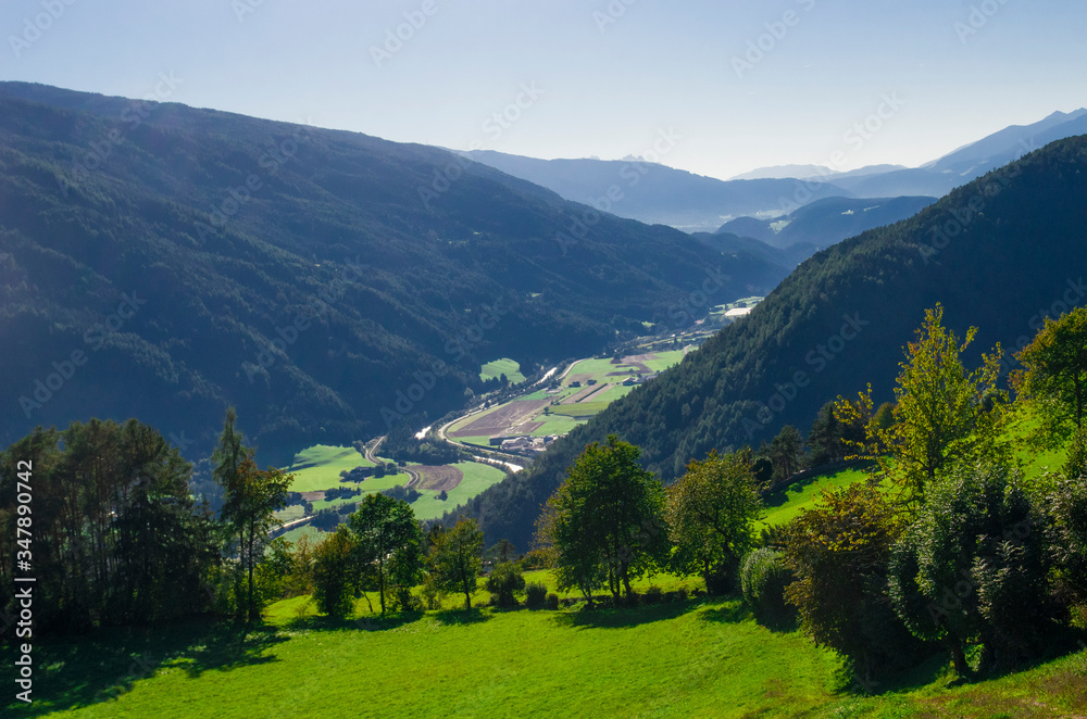 mountain valley with stones and meadows above, lush forests below and below rivers and villages