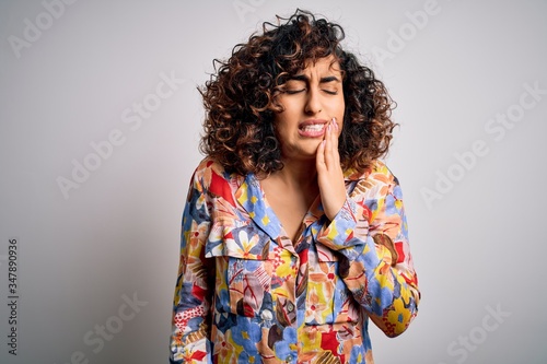 Young beautiful curly arab woman wearing floral colorful shirt standing over white background touching mouth with hand with painful expression because of toothache or dental illness on teeth. Dentist