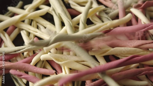 Traditional raw Italian fileja pasta of various colors drops in continuous stream into a pile. Macro shot photo