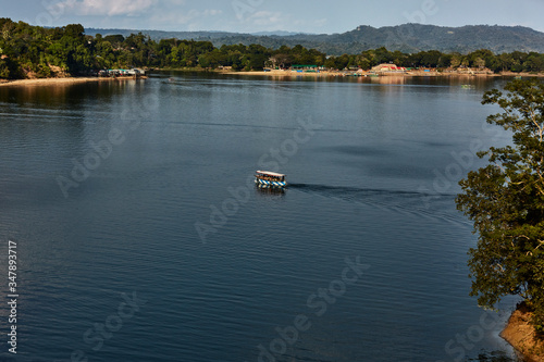 Tourist boat cruises over the calm waters of the Kaptai Lake in a sunny afternoon, Rajasthali, Rangamati, Chittagong Division, Bangladesh - January 05, 2020: cloud-covered knolls under a brilliant sun