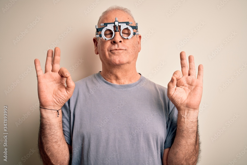 Middle age hoary man controlling vision wearing optometry glasses over white background relax and smiling with eyes closed doing meditation gesture with fingers. Yoga concept. Middle age hoary man controlling vision wearing optometry glasses over white background relax and smiling with eyes closed doing meditation gesture with fingers. Yoga concept.