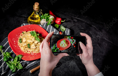 Hands taking photo a tasty appetizing classic italian spaghetti pasta with chicken on dark background with smartphone