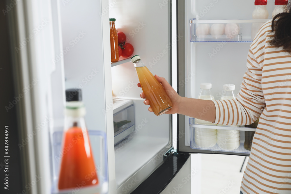 Young woman taking juice out of refrigerator, closeup