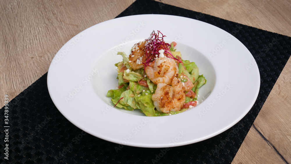 Salad with shrimps on wooden background.