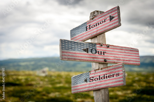 honor our soldiers text on wooden american flag signpost outdoors in nature.