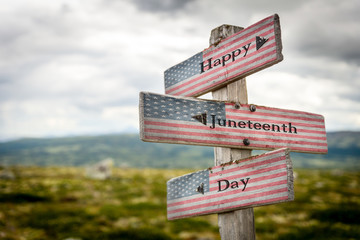 Happy juneteenth day text on wooden american flag signpost outdoors in nature.