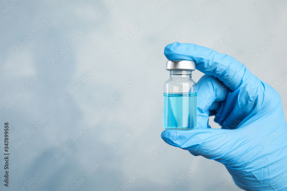 Doctor holding vial with medication on light blue background, closeup view and space for text. Vaccination and immunization Doctor holding vial with medication on light blue background, closeup view and space for text. Vaccination and immunization
