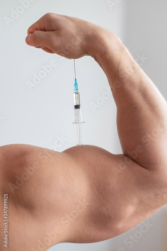 Closeup of a male hand with a dope syringe. Cropped biceps of a man. Unrecognizable bodybuilder sets himself growth hormone testosterone. Vertical photo.