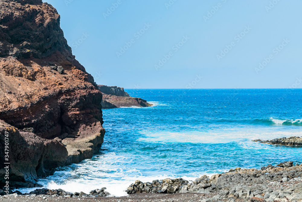 Ocean rocky shore near the cape Teno, Tenerife. Voulcanic rocks with a bright and vibrant blue sea waves. Sunny day on Canary islands