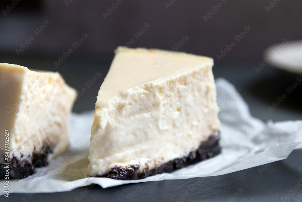 Creamy cheesecake with chocolate cookies slice on baking paper with black tray.