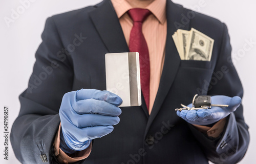 Business man in medical gloves holding credit card and car key, with money in poket, epidemic covi19 photo