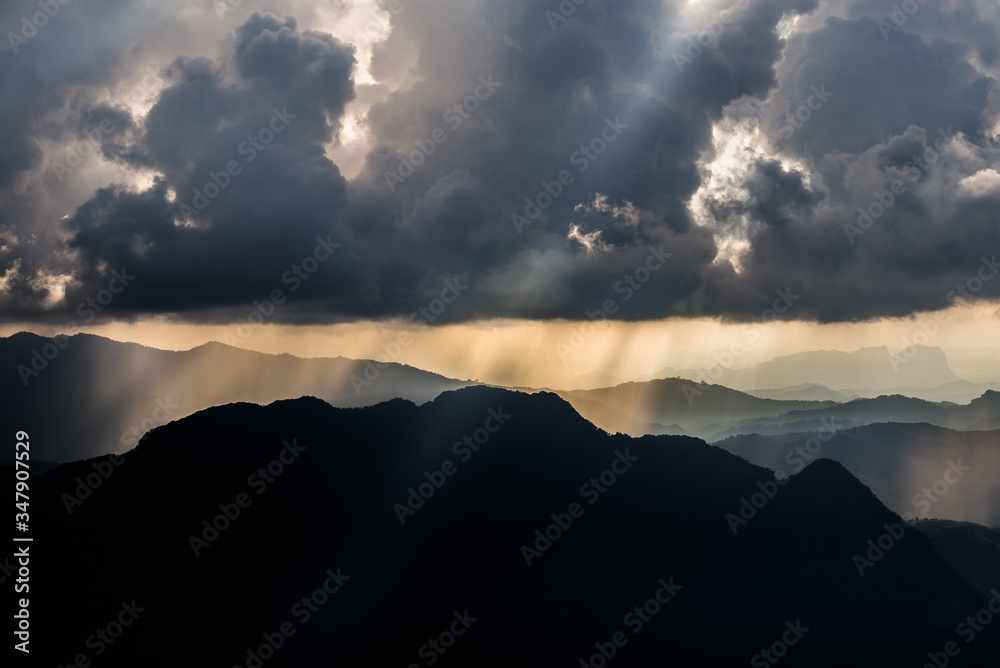 Golden light rays from clouds shining down to mountains. Sun rays over valley. Sun rays over hill. Beam of light from clouds on the mountains. Heaven in nature. Mon Pui Mok, Mae Moei, Tak, Thailand.