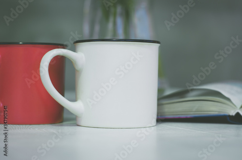Two cups close up. In the background is a book and a vase of flowers. Cup with place for your text.