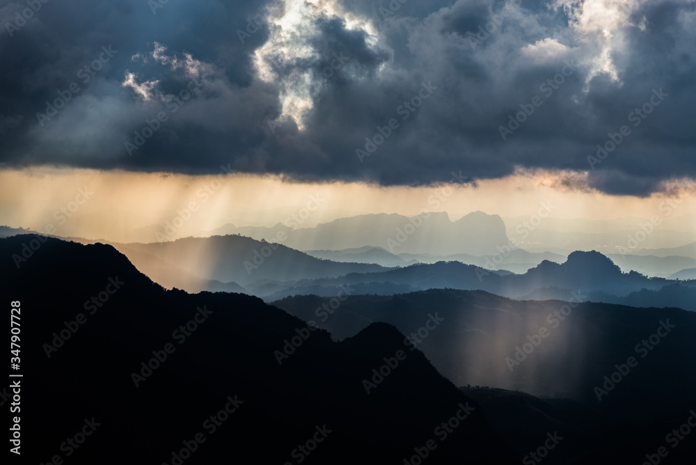 Golden light rays from clouds shining down to mountains. Sun rays over valley. Sun rays over hill. Beam of light from clouds on the mountains. Heaven in nature. Mon Pui Mok, Mae Moei, Tak, Thailand.