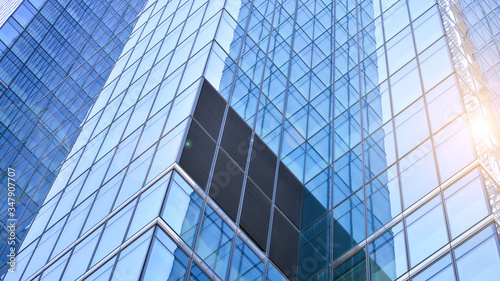 Bottom view of office building window close up with sunrise, reflection and perspective. Modern architecture with sun ray. Glass facade on a bright sunny day with sunbeams on the blue sky. 