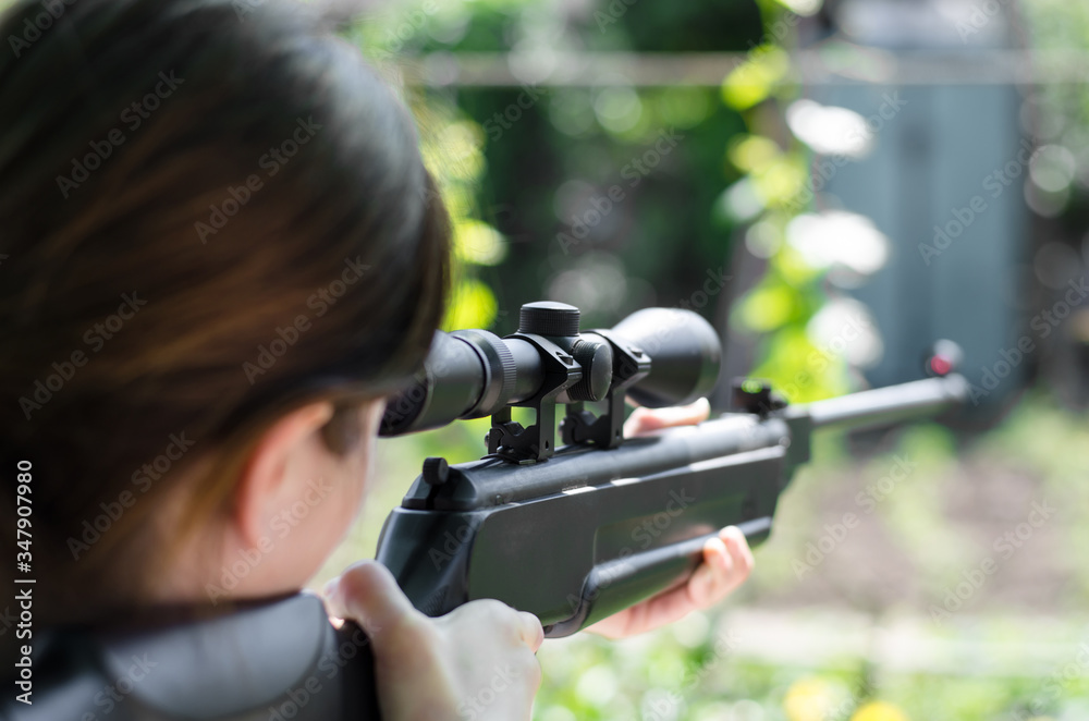 Girl sniper holds a gun in his hands. The hunter is looking into the optical sight from a rear view. Pneumatic gun. looks into the scope of a sniper rifle Girl sniper holds a gun in his hands. The hunter is looking into the optical sight from a rear view. Pneumatic gun. looks into the scope of a sniper rifle