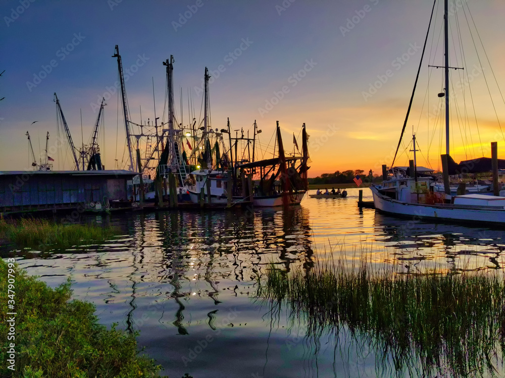 shrimping boats on creek with fishermen motoring by colorful sunset