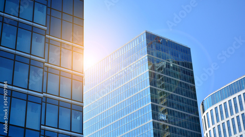 Bottom view of office building window close up with sunrise, reflection and perspective. Modern architecture with sun ray. Glass facade on a bright sunny day with sunbeams on the blue sky. 