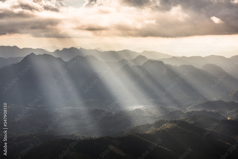 Golden light rays from clouds shining down to mountains. Sun rays over valley. Sun rays over hill. Beam of light from clouds on the mountains. Heaven in nature. Mon Pui Mok, Mae Moei, Tak, Thailand.