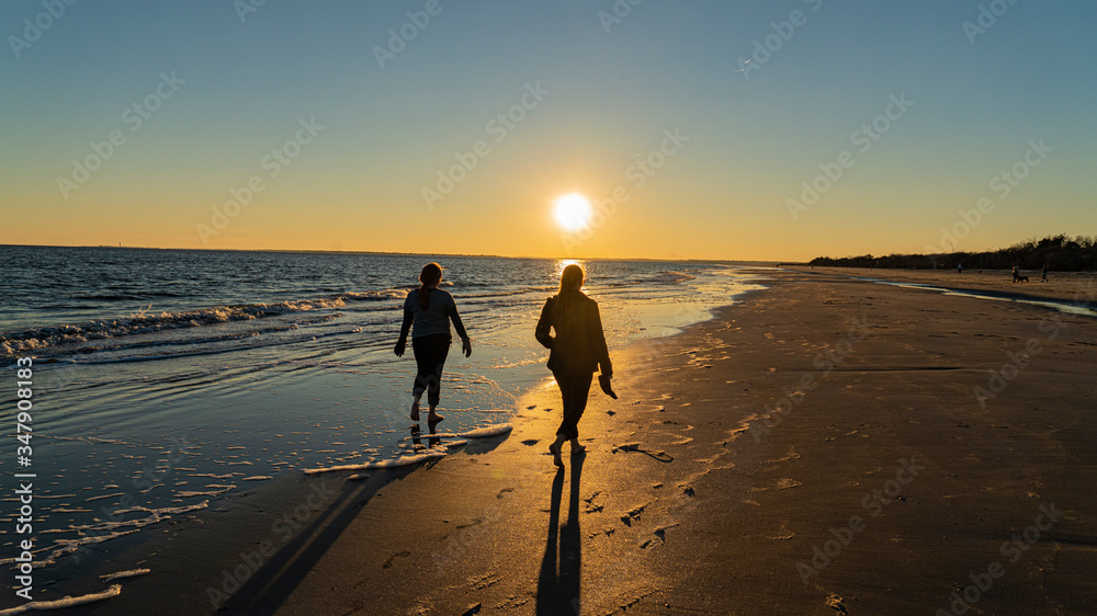 Fototapeta premium silhouetted beach walkers casting long shadows on ocean by cloudless sun