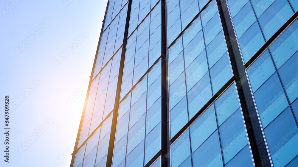 Bottom view of office building window close up with sunrise, reflection and perspective. Modern architecture with sun ray. Glass facade on a bright sunny day with sunbeams on the blue sky. Bottom view of office building window close up with sunrise, reflection and perspective. Modern architecture with sun ray. Glass facade on a bright sunny day with sunbeams on the blue sky.