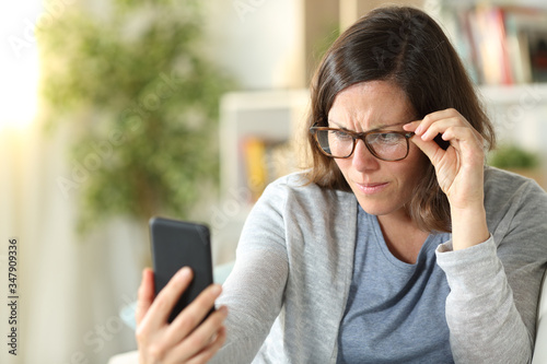Adult woman with eyesight problems reading phone at home photo