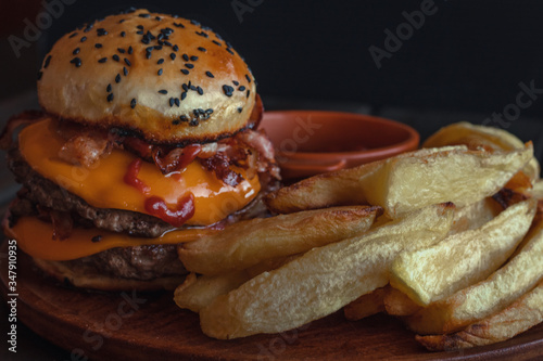 hamburger with french fries, with cheddar cheese, bacon, tomato sauce and mayonnaise on wooden background